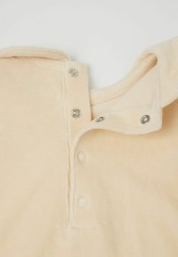 Beżowa bawełniana tkanina z kapturem, z srebrnymi napami przy dekolcie oraz miękką, teksturowaną powierzchnią.