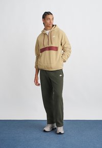 Μπεζ φλις hoodie με βουργουντί οριζόντια ρίγα και τσέπη; συνδυασμένο με ελαιοπράσινα παντελόνια φόρμας και γκρι αθλητικά παπούτσια. Απλός, casual σχεδιασμός.