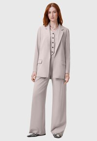 Completo grigio chiaro su misura con giacca lunga, pantaloni a gamba larga e un gilet con bottoni scuri. Tessuto liscio con una finitura lucida.