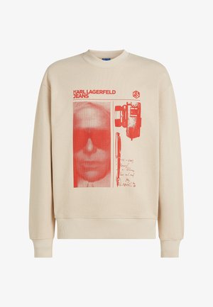 Beež pusa, millel on punase trükiga näokuju päikeseprillidega, pastakas ja käsitsi kirjutatud tekst. Soonikkoes äär ja varrukasäärmed.