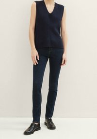 Laivastonsininen hihaton neulepaita V-pääntiellä, jossa on kohokuvioitu vinokuvio. Yhdistetty tummiin farkkuihin ja mustiin nauhallisiin kenkiin.