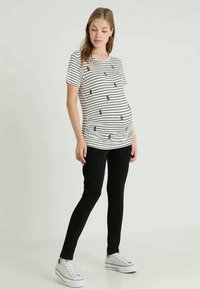 T-shirt de maternidade com riscas horizontais pretas e brancas, com pequenos detalhes dourados. Combinado com leggings pretas e ténis brancos.