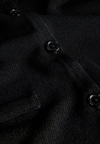 Κοντινή λήψη μαύρου υφασμάτινου με υφή με τρία γυαλιστερά μαύρα κουμπιά ραμμένα σε κάθετη σειρά.