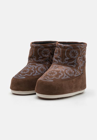 Brown suede boot slippers featuring floral embroidery in light blue. Low-cut design, rounded toe, and a white rubber sole.