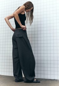 Wijdvallende broek in donkergrijs met verticale streepjes, voorzien van een enkele achterzak en een gladde textuur, gecombineerd met zwarte ballet flats.