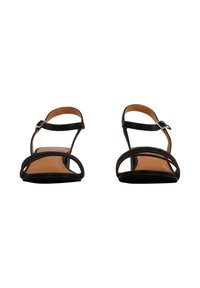Sandalias negras de tiras con suela plana y una correa ajustable en el tobillo. Presentan un diseño simple y una textura de cuero suave.