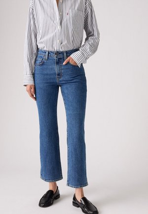 Jeans en denim bleu avec une coupe droite et un ourlet effiloché. Associés à une chemise à rayures bouton-nue et des mocassins noirs.
