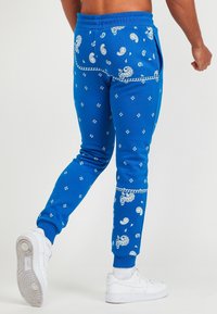 Niebieskie spodnie dresowe z wzorami paisley i diamentowymi, elastycznym paskiem w talii oraz ściągaczami przy nogawkach. Połączone z białymi trampkami dla kontrastu.