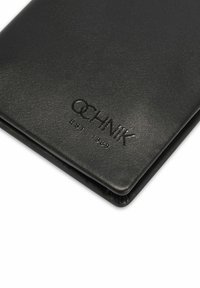 Czarny skórzany portfel o teksturowanym wykończeniu, z tłoczonym logo „OCHNIK” oraz napisem „EST. 1989.” Kompaktowy, prostokątny kształt z zaokrąglonymi rogami.