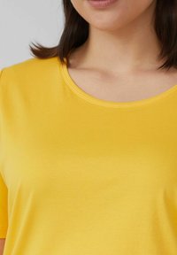 Gelbes kurzärmliges Oberteil mit rundem Ausschnitt, aus einem glatten Stoff gefertigt und mit einem einfachen, ungeschmückten Design.