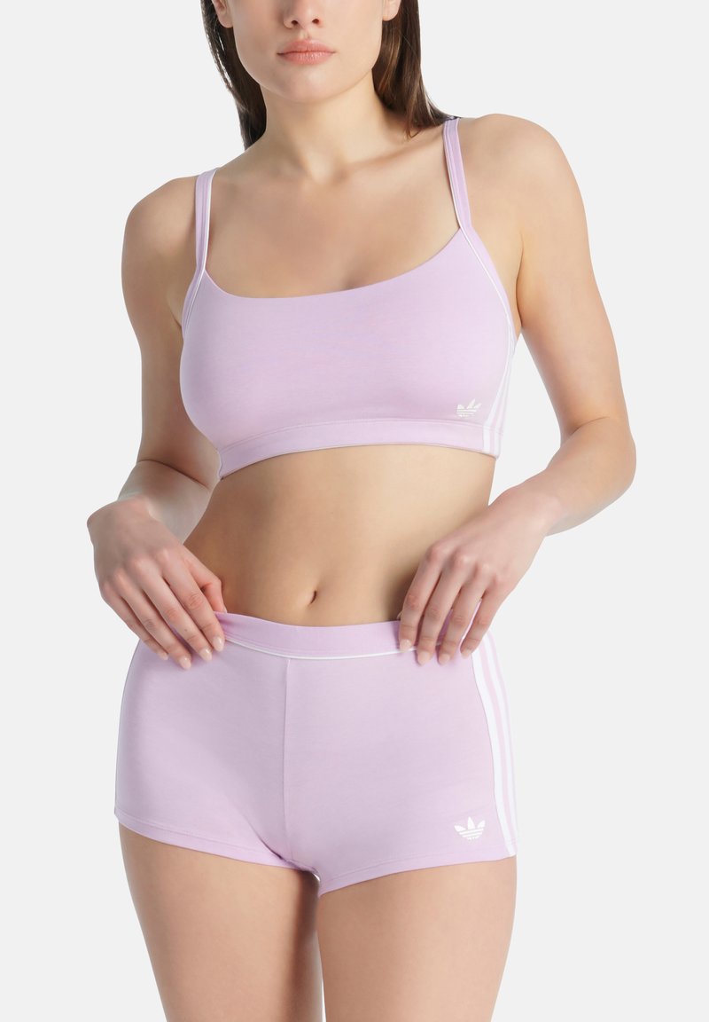 Fialová sportovní podprsenka s tenkými ramínky a odpovídajícími šortkami, s bílými bočními pruhy a logem Adidas. Hladká, elastická tkanina, atletický design.