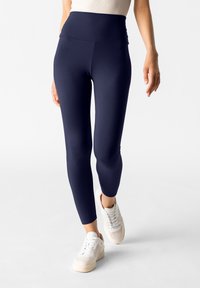 Leggings a vita alta di colore blu navy realizzati in un tessuto liscio e elastico, con una vestibilità affusolata e cuciture pulite, abbinati a scarpe da ginnastica bianche.