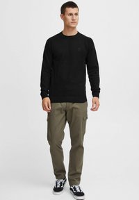 Black knitted pullover with a crew neck, paired with olive cargo pants featuring pockets. Footwear is black and white sneakers.