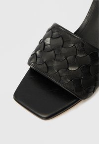 Μαύρο δερμάτινο σανδάλι τύπου slide με πλεγμένο σχέδιο λουριού, υφή στην επιφάνεια και τετράγωνη μύτη. Λείο, ματ φινίρισμα στη σόλα.