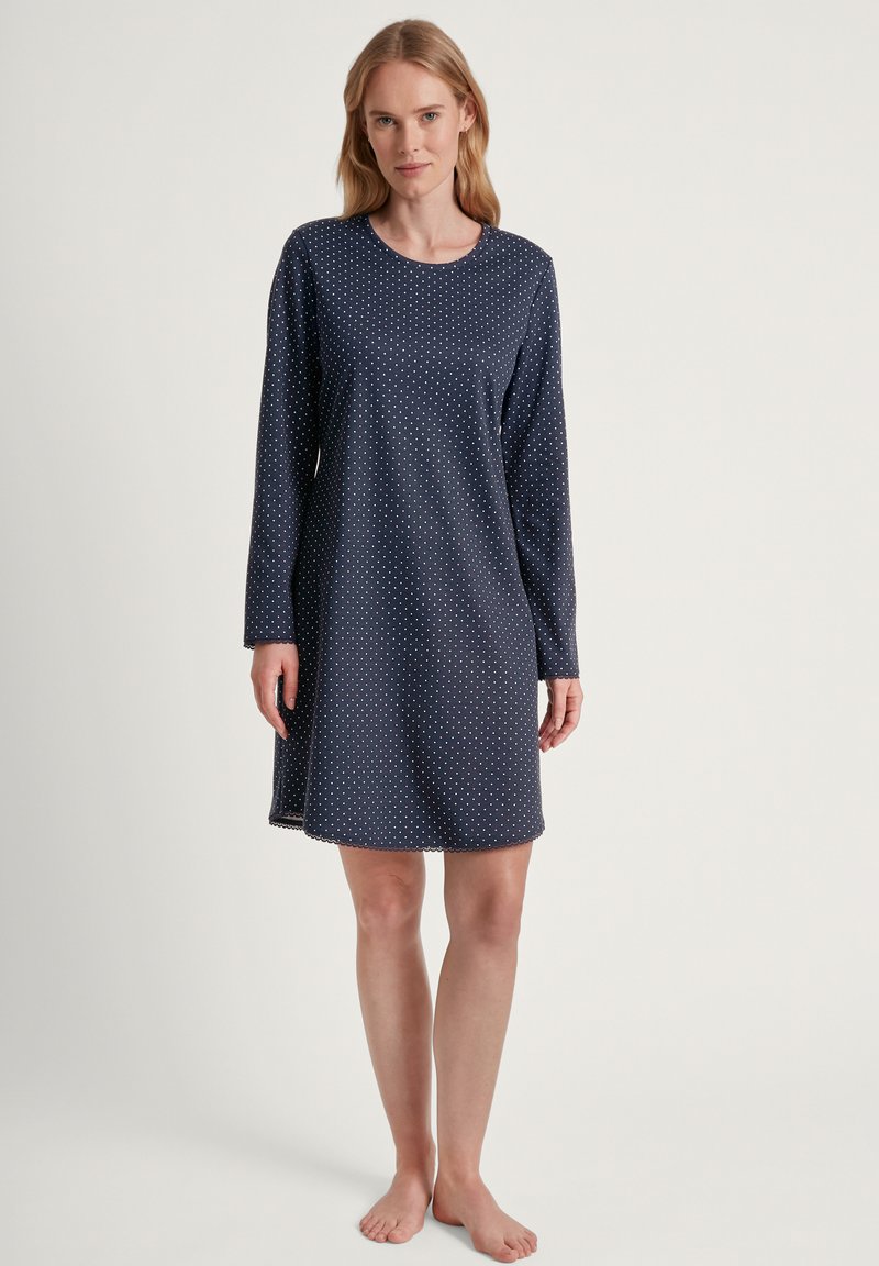 Chemise da notte blu navy con maniche lunghe, decorata con pois bianchi, scollatura rotonda e orlo ondulato. Realizzata in tessuto morbido.