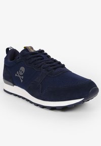 Navyblauwe sportshoe met een bovenwerk van textiel en suède, rubberen zool, vetersluiting en een schedelgrafiekdetail aan de zijkant.