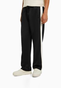 Black track pants featuring a sleek design with contrasting white side stripes. Made from a smooth fabric with an elastic waistband and drawstring.