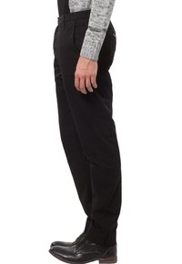 Černé kalhoty z hladké bavlněné látky, s úzkým střihem a bočními kapsami, doplněné lesklými černými botami.