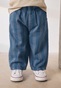 Modre hlače z belimi črtami, elastičnim pasom in ohlapnim krojem, kombinirane z belimi supergami z rdečimi poudarki in teksturiranimi podplati.