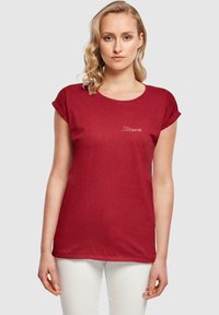 Rød kortærmet t-shirt lavet af blødt stof, med rund halsudskæring og en lille hvid hjerte og tekstdetalje på forsiden.
