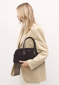 Black suede handbag with leather handles and a zip closure. Features a curved design and a logo on the front.