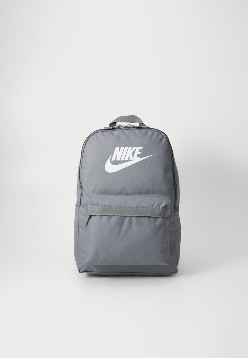 Mochila Nike cinza com um bolso frontal, fecho de correr e logótipo em branco. O material parece durável e texturizado, apresentando uma forma retangular.