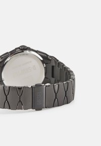 Schwarze Metallarmbanduhr mit einem dehnbaren Gliederarmband. Verfügt über einen polierten silbernen Gehäuseboden und einen Verschluss mit eingraviertem "DIESEL".