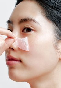 Patch adhésif transparent à surface texturée appliqué sur le côté du nez d'une personne. Peau lisse et maquillage naturel visibles.