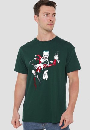 Man wearing dark green t-shirt with graphic of two stylized comic characters dancing, one in red and black costume and one in white suit.