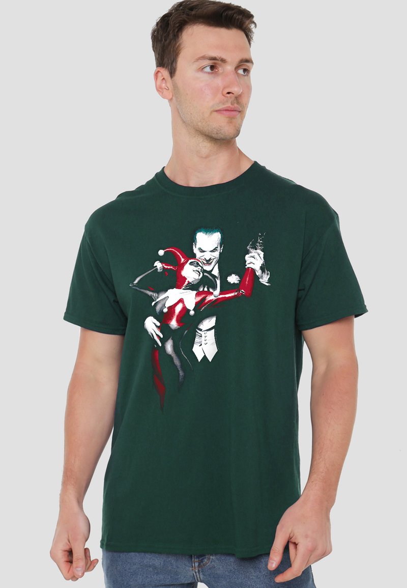 Man wearing dark green t-shirt with graphic of two stylized comic characters dancing, one in red and black costume and one in white suit.