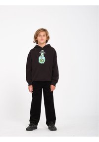 Zwarte hoodie met een grafisch alienontwerp in het groen, gecombineerd met zwarte corduroy broek en zwarte sneakers. Eenvoudige, casual outfit.