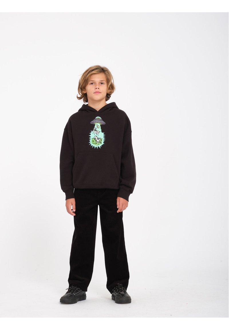 Zwarte hoodie met een grafisch alienontwerp in het groen, gecombineerd met zwarte corduroy broek en zwarte sneakers. Eenvoudige, casual outfit.