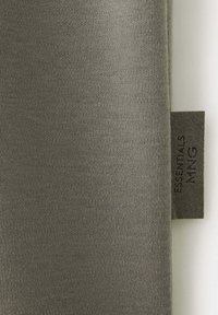 Gros plan sur un tissu en maille gris avec une petite étiquette gris foncé portant la mention "ESSENTIALS MYNG" cousue dans la couture sur le côté droit.