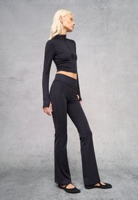 Zwart sportoutfit met een ritscropped top en uitlopende broek, gemaakt van gladde stof met een aansluitende pasvorm en naadloze randen.