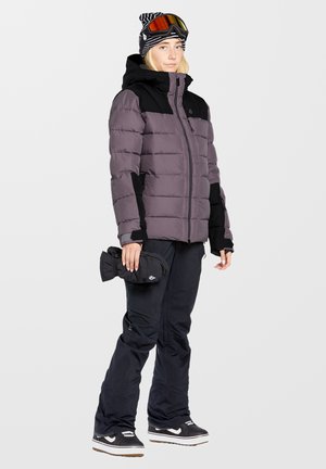 Purple and black puffy jacket with a zip front, black ski pants, and black gloves. Striped beanie with goggles completes the winter outfit.