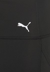 Leggings sportivi neri con materiale testurizzato, dotati di un logo Puma bianco sul lato sinistro e dettagli delle cuciture in vista.