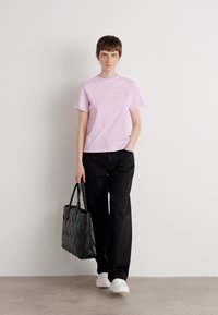 Camiseta de algodón de color púrpura claro con cuello redondo, pantalones de pierna ancha negros y un bolso tote negro texturizado. Zapatillas blancas completan el atuendo.