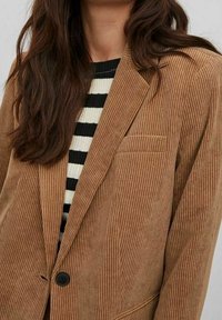 Hnědý kordurový blazer s vertikální žebrovanou texturou, s jedním knoflíkem a náprsní kapsou. Nosený přes černo-bíle pruhovaný top.