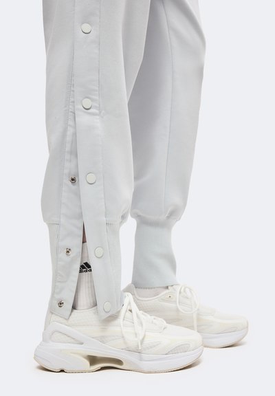 Unterschenkel, die hellgraue Hosen mit Druckknöpfen und weiße Sneakers mit dicken Sohlen sowie weiße Socken tragen.