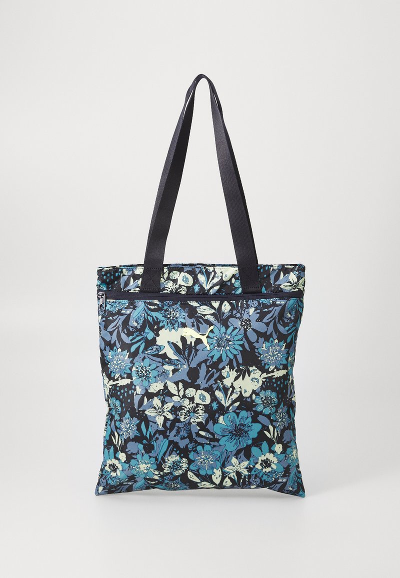 Floral tote bag in navy fabric featuring blue and light green flower patterns. Two sturdy black straps for carrying. Zippered top closure.