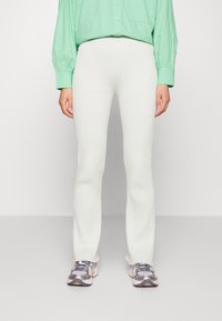 Calças de malha branca com nervuras e bainha flare, combinadas com ténis cinzentos e rosas e uma camisa oversized azul clara com botões.