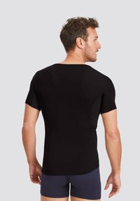 Black short-sleeve shirt with round neckline, fitted style, smooth fabric, and side panel design. Model shown from the back.