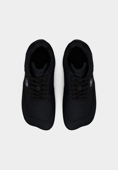 Ζευγάρι μαύρα αθλητικά παπούτσια με κορδόνια, στρογγυλεμένες μύτες και μικρό λευκό τυπωμένο λογότυπο στα πλάγια, από πάνω σε λευκό φόντο.