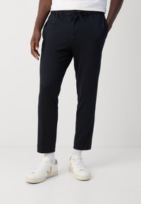 Granatowe spodnie dresowe ze ściągaczem w pasie, bocznymi kieszeniami i zwężanym krojem. Do tego białe trampki i prążkowane białe skarpetki.