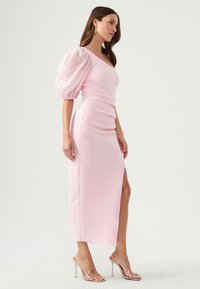 Pink midi dress with textured fabric, featuring puff sleeves made of sheer material with polka dots and a side slit.