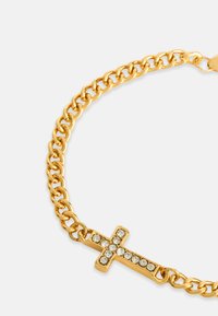 Brățară din lanț de aur, cu un pandantiv în formă de cruce, decorat cu strasuri clare, având o textură netedă și zale interconectate.