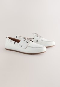 Hvide læder bådsko med rund tå, flad gummisål og snøredesign. Har sorte snørehuller og cremefarvede accenter på overdelen.