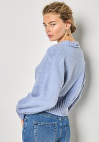 Jasnoniebieski sweter dziany z prążkowanym dołem i oversize'owymi rękawami. Noszony z niebieskimi dżinsami o wysokim talerzu. Luźny krój i miękka tekstura.