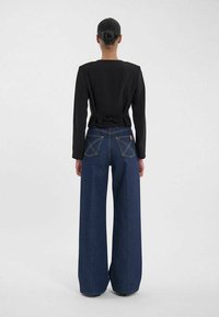 Haut noir à manches longues avec détail de lien dans le dos, associé à un jean en denim foncé à jambes larges avec des coutures contrastantes et un design de poche arrière distinctif.