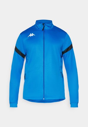 Mėlyna sportinė striukė su aukštu apykakle, pilnu priekiu užtrauktuku, juoda peties juosta ir dviem užtrauktukais uždaromomis šoninėmis kišenėmis. Lygus medžiagos paviršius.